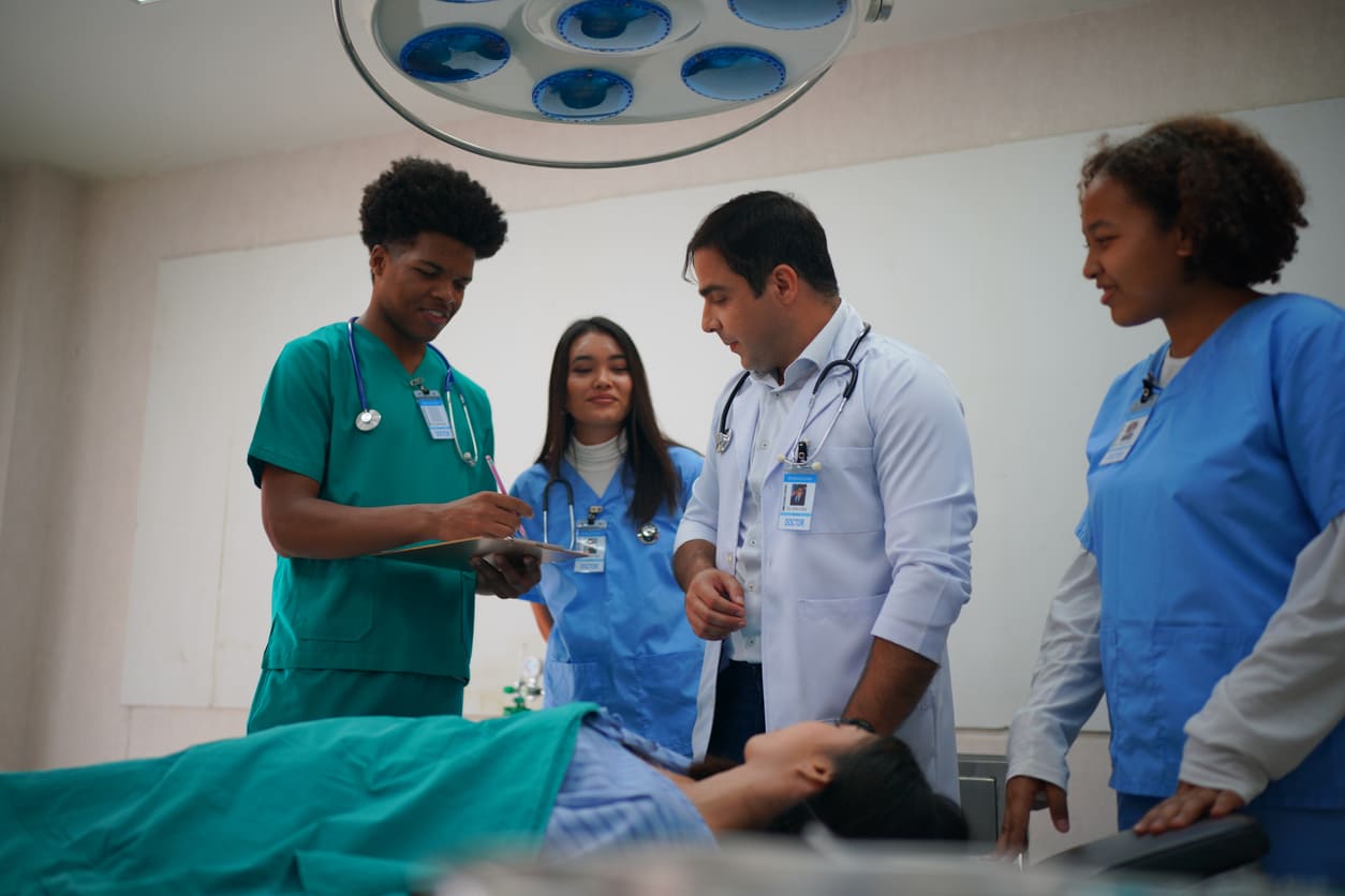 Equipe médica em centro de saúde realizando avaliação de paciente deitada na maca, com profissionais atentos e equipamentos hospitalares ao fundo.