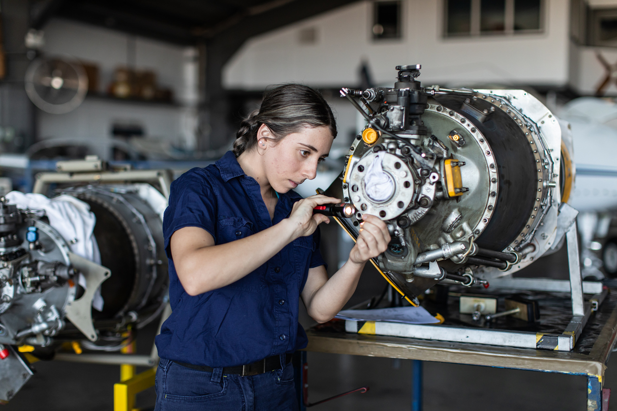 Engenheira trabalhando em motor de aeronave em oficina de manutenção aeronáutica